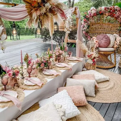 This stunning boho-themed baby shower is perfect for a stylish mom-to-be. The setup includes a peacock chair, low picnic seating with plush cushions, and beautiful dried floral arrangements.