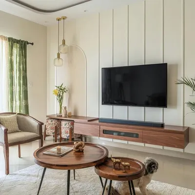 This living room from my Sobha Daffodil project balances classic and contemporary elements. A floating wooden TV unit is set against a wall with modern vertical paneling and a soft arch, creating a serene and elegant focal point.