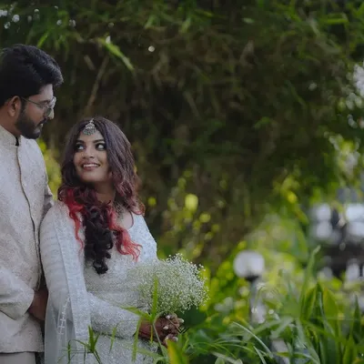 A stylish couple posing in a lush, green outdoor setting, showcasing a modern yet romantic look.