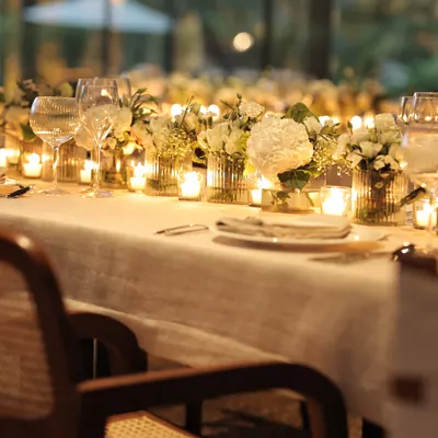 A long table dressed in white linen and bathed in candlelight creates a truly magical setting for a sit-down dinner. The rows of candles and white flowers reflect our philosophy of simple, timeless elegance.