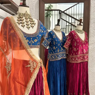 A stunning display of lehengas in jewel tones. The foreground features a blue embroidered blouse with a contrasting orange and pink skirt, perfect for a wedding guest.