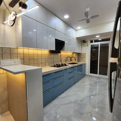 A stunning parallel kitchen from a completed project, featuring powder blue and white high-gloss acrylic cabinets, a breakfast counter with fluted paneling, and modern pendant lights. This is a perfect example of our turnkey kitchen solutions.