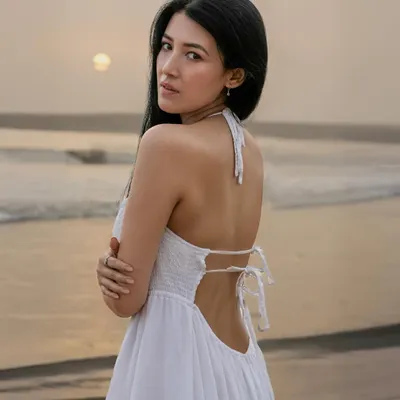 A beautiful back-shot of a model in a white dress against the setting sun. This image captures the serene and peaceful atmosphere of the beach at dusk.