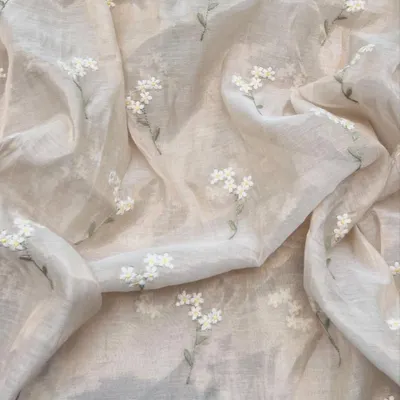 This Chanderi tissue fabric is as light as air. It features delicate white floral sprigs embroidered on a translucent beige background, creating a look of pure, understated sophistication for a saree or dupatta.