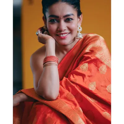 A warm and joyful portrait in a vibrant orange saree. The yellow background and the subject's bright smile create an image that is full of life and color, celebrating traditional Indian fashion.