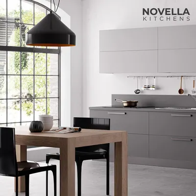 A minimalist grey kitchen set against a large window, creating a bright and airy cooking space. The simple wooden dining table complements the clean design of the modular units.