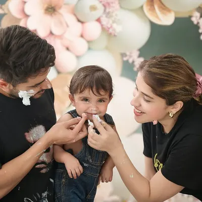 The whole family joins in on the fun! This candid shot captures the parents playfully sharing a bit of cake with their child during a first birthday cake smash session.