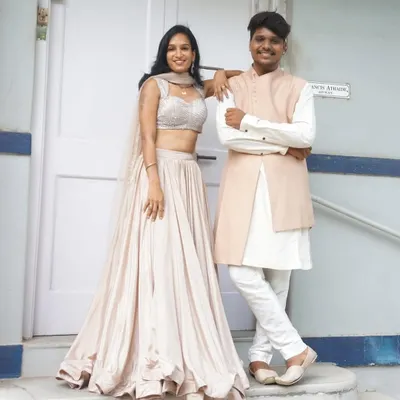 A classic his and her look. She’s in a flowing satin lehenga with a sequin blouse, and he’s in a complementary peach bandhgala jacket over a white kurta. Simple, elegant, and perfectly coordinated.