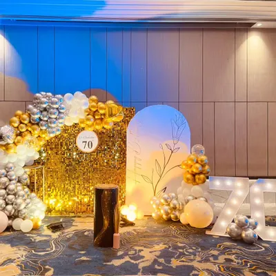 A glamorous 70th birthday celebration featuring a gold sequin shimmer wall, a silver and gold balloon arch, and large light-up marquee numbers.