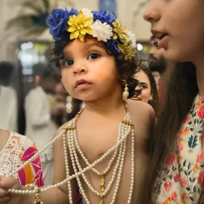 A close up portrait of a young child dressed as Lord Krishna for Janmashtami, looking directly into the camera with wide, innocent eyes.