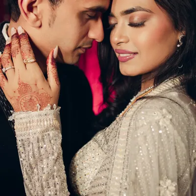 An intimate close-up capturing the tender chemistry between the couple. The focus on the bride's henna-adorned hand gently touching his neck adds a layer of traditional romance to this modern, glamorous shot.