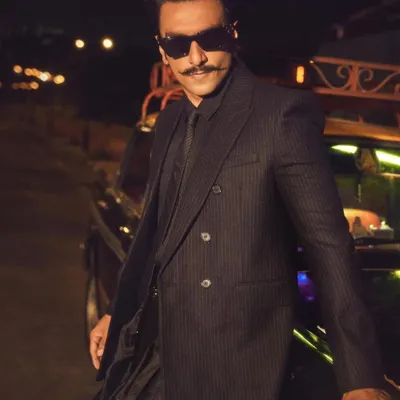 Ranveer Singh embodying the 'Desi Kalakar' vibe for the Jio World Plaza opening. This look features a sharp pinstripe YSL blazer paired with draped Manish Malhotra pants and boots, creating a fusion of global and Indian aesthetics.