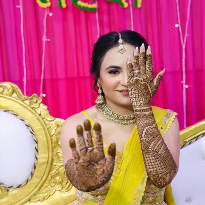 A classic mehndi pose! The bride shows off her intricate henna, and the makeup is kept fresh and bright with pink tones to complement her yellow outfit.