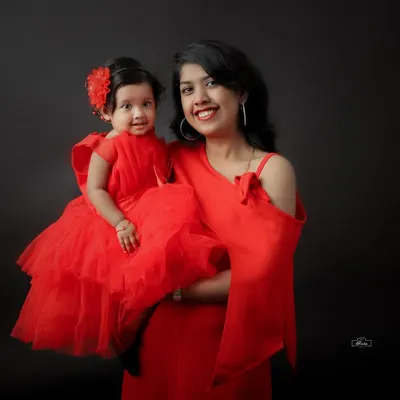 A striking mother and daughter portrait with matching red dresses against a classic dark backdrop. This studio shot emphasizes connection and style, creating a bold and beautiful memory.
