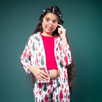 This portrait is all about confidence and style. Her cool pose, patterned outfit, and tinted glasses create a look that is both playful and fashion-forward. The solid teal background makes her vibrant personality pop right out of the frame.