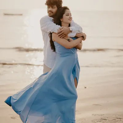A beautiful golden-hour portrait on the beach, with the wind catching the bride's dress as the couple embraces by the sea.