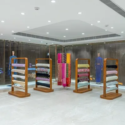 The unstitched fabric section in the Nalli showroom, featuring custom-designed wooden display racks. These fixtures are designed for flexibility, with adjustable shelving that allows for stacking, hanging, or mannequin displays within the same unit.