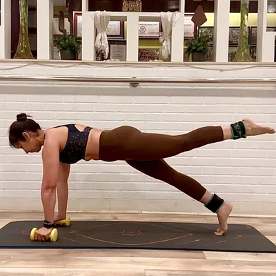 Pilates is about precision and control. Here, I am holding a plank with a leg lift, using ankle weights for added resistance and light dumbbells to engage my arms and shoulders. This single pose is a full-body exercise that strengthens the core, glutes, and upper body simultaneously.