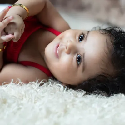 A beautiful close-up of a happy baby girl with sparkling eyes and curly hair, lying on a soft white rug.