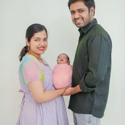 A classic family portrait with both parents holding their newborn. The clean white background keeps the focus entirely on the family's happy moment together.