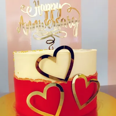 A beautiful and modern anniversary cake in red and white, adorned with elegant gold hearts and a script topper. A perfect centerpiece for a love-filled celebration.