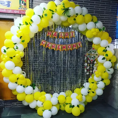 A fun and modern backdrop for a Haldi ceremony. This setup features a large circular frame made of yellow and white balloons with a silver fringe curtain in the center.