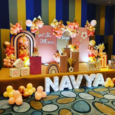 A "Boho Rainbow" themed first birthday party for Navya. This stage setup features pastel balloon arrangements, a custom backdrop, and large marquee lights for the number '1' and the name.