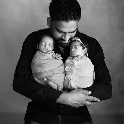 A new father holds his twin newborn babies, one in each arm. This powerful black and white portrait captures the overwhelming love and pride of a dad on Father's Day.