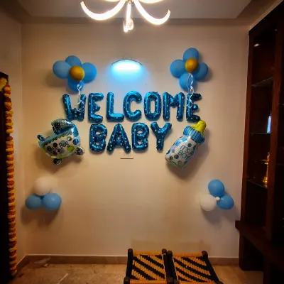 A simple 'Welcome Baby' decoration for a home. This includes a blue foil balloon banner and other small balloon accents like a bottle and an airplane.
