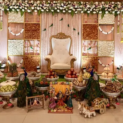A complete view of a grand Seemantha setup, featuring a beautiful backdrop with jasmine and marigold panels. The foreground is filled with an elaborate display of traditional sweets and fruits on silver stands, creating a picture of abundance.