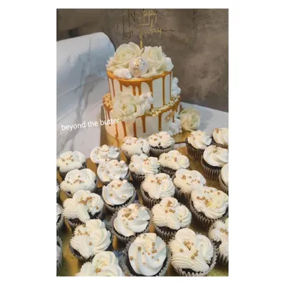 This elegant white and gold drip cake is paired with a large order of matching cupcakes. The cupcakes are topped with white buttercream and gold sprinkles, creating a stunning dessert display for any celebration.