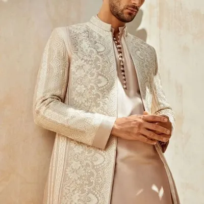 A model showcases a sophisticated off-white sherwani jacket with intricate self-colored embroidery. This piece is a perfect example of understated elegance, ideal for the modern groom who appreciates fine craftsmanship.