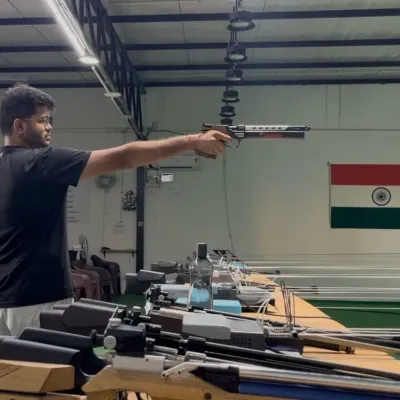 A shooter demonstrates a perfect one-handed stance during air pistol training, with the Indian flag symbolizing the ultimate goal.