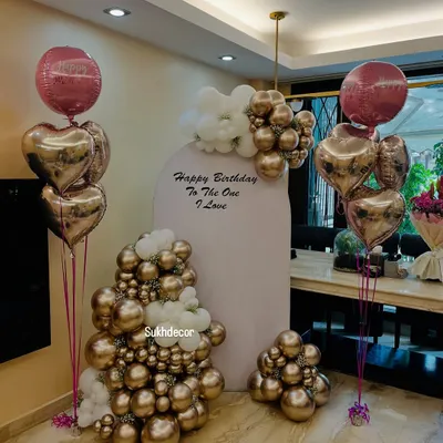 An elegant birthday backdrop featuring a large arch panel with the message 'Happy Birthday To The One I Love'. The setup is decorated with beautiful chrome gold and white balloon arrangements and heart-shaped foil balloons.
