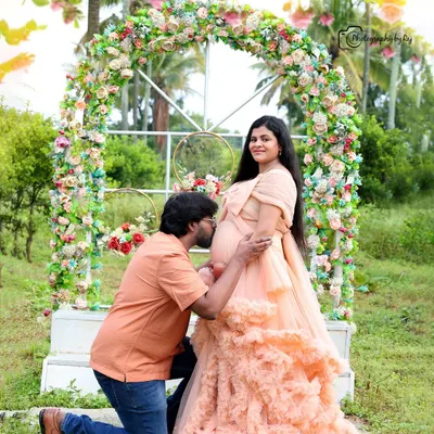 A beautiful couple's portrait under a vibrant floral arch. The partner's gentle kiss on the baby bump is a classic pose that captures the love and excitement of this special time.