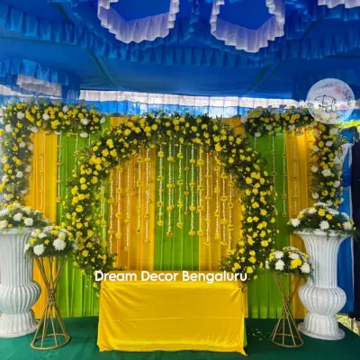 A classic Haldi decor with a vibrant yellow and green backdrop. The floral arch made of yellow chrysanthemums and hanging marigold strings creates the perfect festive mood.