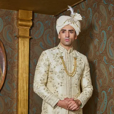 An ivory and gold sherwani is the epitome of classic groomswear. This piece features delicate, all-over floral embroidery, paired with a matching safa and a traditional gold necklace for a truly royal look.