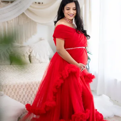 A vision in red. This mom-to-be radiates joy in one of our ruffled tulle gowns, complemented by a delicate crown and our bright, airy studio backdrop.