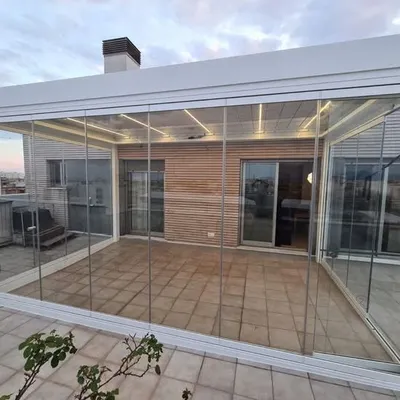 A complete rooftop sunroom constructed with sliding glass panels and a fixed glass roof. This enclosure creates a usable, light-filled room on the terrace, protected from wind and rain.