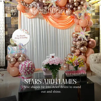 Stars and flames for an Aries celebration. This rose gold and peach setup is perfect for someone who loves to shine, featuring a beautiful balloon garland, floral arrangements, and a cozy, elegant seating area.