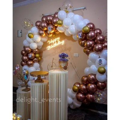 An elegant and popular choice, this full circular balloon arch combines metallic rose gold and classic white balloons. It's paired with a neon 'Happy Birthday' sign and fluted pedestals, creating a chic and modern photo corner.