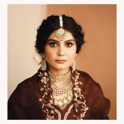 A classic bridal portrait that captures a moment of quiet reflection. We styled this look with heavily layered polki and pearl necklaces, a traditional maang tikka, and a rich maroon outfit to create a vintage, almost Mughal-inspired aesthetic.