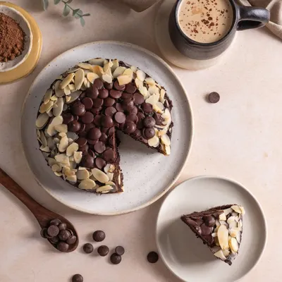 A top-down shot of a rich chocolate almond cake, with a slice cut out to show the texture inside. This flatlay style is perfect for menus and social media, showing the cake, a coffee, and the ingredients.
