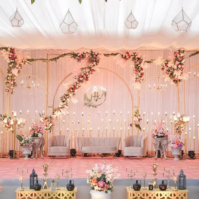 A truly regal reception stage in blush pink tones. The setup features elegant seating, cascading floral arrangements, and delicate candle lighting, all framed by custom golden arches for a majestic feel.