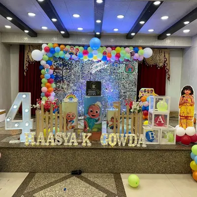 A fantastic Cocomelon stage for a fourth birthday. This setup features a silver shimmer wall, a rainbow balloon arch, character cutouts, and a large marquee number '4'.