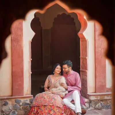 Framed by a traditional archway, this quiet moment captures the regal elegance of a palace romance. The couple's coordinated ethnic wear complements the heritage architecture perfectly.
