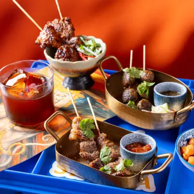 A selection of Asian-inspired appetizers for Banng, served in traditional brass bowls against a bold blue and orange background.