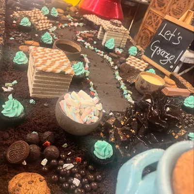 A close-up of our whimsical chocolate grazing table, featuring a landscape of chocolate soil, wafer houses, marshmallows, and cupcakes.