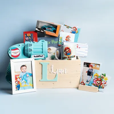 A complete, custom-curated gift hamper for a child's birthday. This one features a personalized Peter Pan book, a Mario-themed mug, toys, and a custom wooden crate with the child's initial.