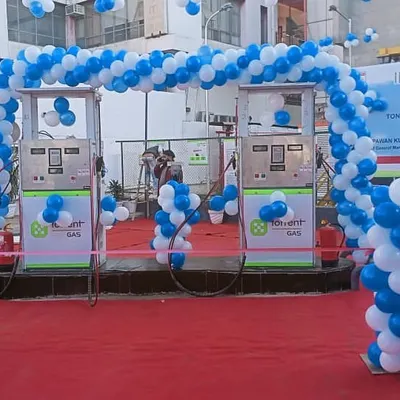 An inauguration event for a new CNG station. A classic blue and white balloon arch frames the fuel pumps, adding a festive touch to the official launch.